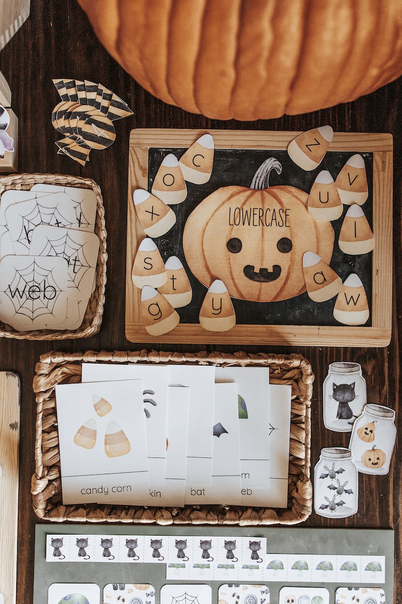 May include: A Halloween-themed educational set with a pumpkin, candy corn, and alphabet letters. The set includes flashcards with words like "web" and "candy corn", and decorative jar cutouts. The word "lowercase" is written on the pumpkin.