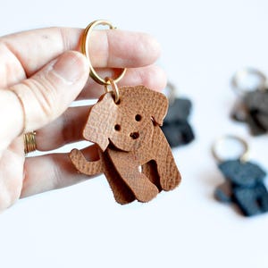 May include: A brown leather dog keychain with a gold key ring. The dog is standing on all four legs and has a cute face.