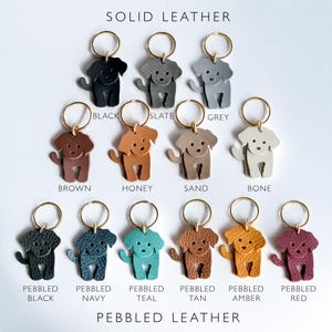 May include: A collection of dog-shaped keychains in various colors, including black, grey, brown, honey, and teal. The keychains are made of solid and pebbled leather, each with a gold-colored keyring. The text "SOLID LEATHER" and "PEBBLED LEATHER" are displayed.
