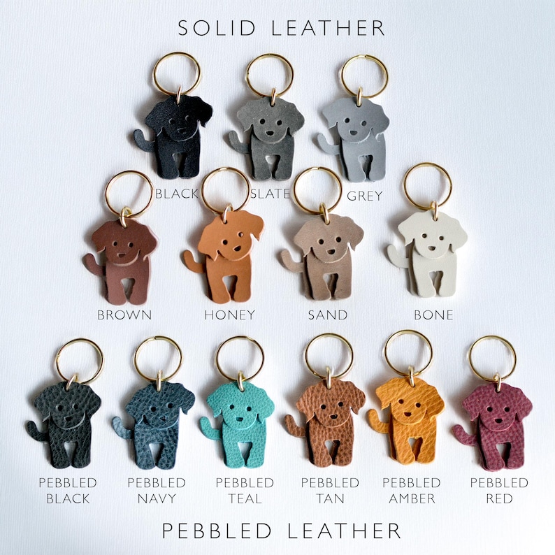 May include: A collection of dog-shaped keychains in various colors, including black, grey, brown, honey, and teal. The keychains are made of solid and pebbled leather, each with a gold-colored keyring. The text "SOLID LEATHER" and "PEBBLED LEATHER" are displayed.