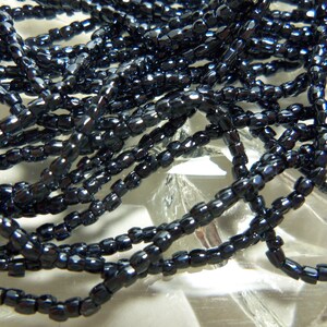 May include: A strand of black seed beads, with a slightly iridescent finish. The beads are small and uniform in size, and they are strung together on a clear thread.