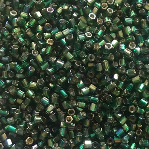 May include: A close-up image of a large quantity of small, dark green iridescent glass beads. The beads are hexagonal in shape and have a metallic sheen.