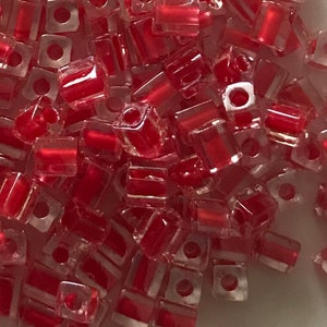 May include: A pile of red and clear glass square beads. The beads are translucent and have a shiny finish.