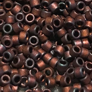 May include: A close-up of a pile of small, round, brown beads with a metallic sheen. The beads are arranged in a random pattern, and some of them are slightly out of focus.