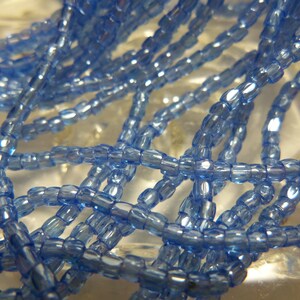 May include: A strand of light blue glass seed beads. The beads are small and have a slightly iridescent finish.