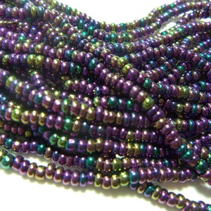 May include: A strand of iridescent seed beads in shades of purple, green, and gold. The beads are small and round, and they have a metallic sheen.