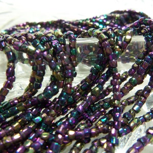 May include: A strand of iridescent purple, green, and gold seed beads. The beads are small and square shaped.