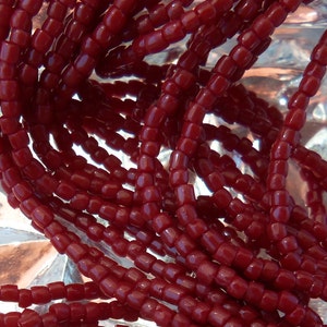 May include: A close-up of a pile of red glass beads. The beads are small and round, and they are arranged in a random pattern.