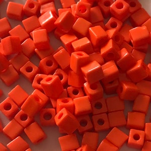 May include: A large pile of bright orange square beads with a hole in the center of each bead.
