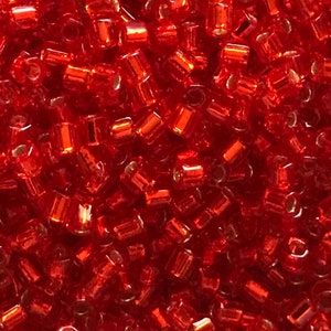 May include: A close-up image of a large quantity of small, red, glass beads. The beads are cylindrical in shape and have a shiny, metallic finish.