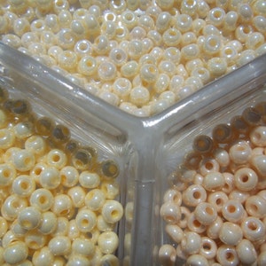 May include: Three clear plastic containers filled with white and cream colored round beads. The beads are arranged in a triangular pattern.