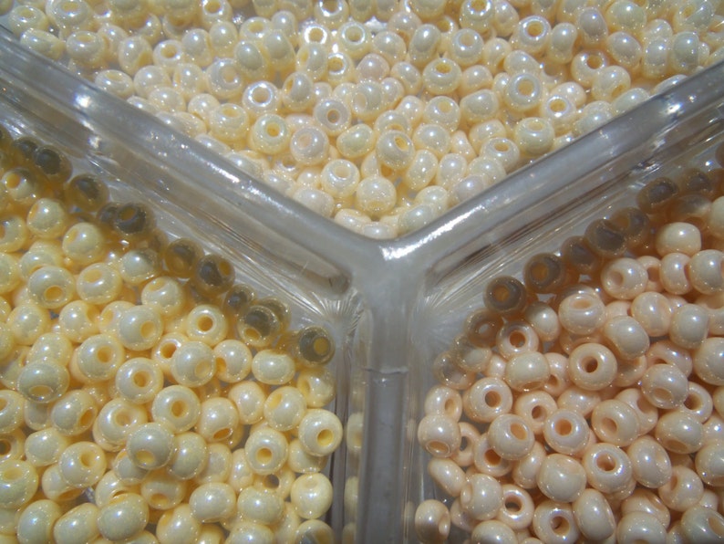 May include: Three clear plastic containers filled with white and cream colored round beads. The beads are arranged in a triangular pattern.