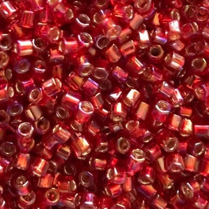 May include: A close-up image of a large quantity of small, red, iridescent glass beads. The beads are hexagonal in shape and have a shiny, metallic finish.