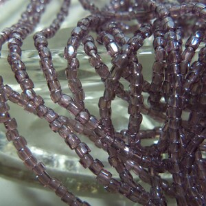 May include: A strand of small, light purple glass beads. The beads are cylindrical and have a slightly iridescent finish.