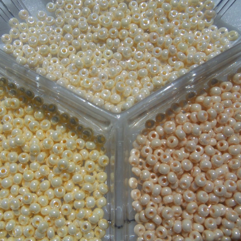 May include: Three divided compartments filled with white and cream colored seed beads. The beads are small and round.