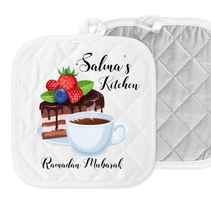 May include: White quilted pot holder with a design of a slice of chocolate cake with berries and a cup of coffee. The text "Salma's Kitchen" and "Ramadan Mubarak" are printed on the pot holder.