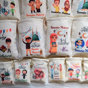 May include: A collection of 12 small drawstring bags with various designs featuring cartoon children, Islamic calligraphy, and the phrase "Ramadan Mubarak". Some bags also include the phrase "Eid Mubarak".