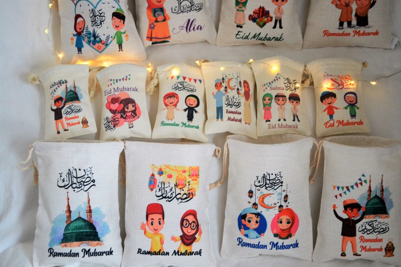May include: A collection of 12 small, white drawstring bags with various colorful designs featuring cartoon children, Islamic calligraphy, and the phrases "Ramadan Mubarak" and "Eid Mubarak".