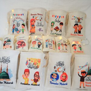 May include: Assortment of colorful drawstring bags with various Ramadan and Eid Mubarak designs. The bags feature illustrations of people, mosques, and lanterns. Some bags have the text "Ramadan Mubarak" or "Eid Mubarak" printed on them.