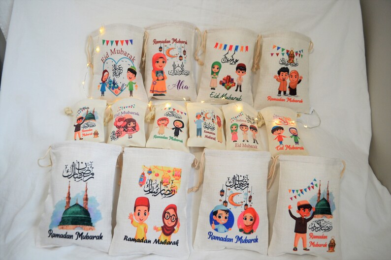 May include: Assortment of colorful drawstring bags with various Ramadan and Eid Mubarak designs. The bags feature illustrations of people, mosques, and lanterns. Some bags have the text "Ramadan Mubarak" or "Eid Mubarak" printed on them.