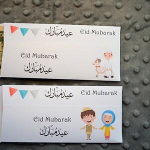 May include: Two white envelopes with colorful flags and Arabic text that says "Eid Mubarak". The envelopes have illustrations of children celebrating Eid. One envelope has a boy holding a lamb and the other has a boy and girl holding hands.