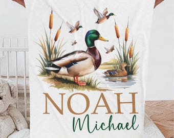May include: White baby blanket with a green, brown, and white mallard duck illustration. The blanket has the name "NOAH Michael" printed in brown and green text.