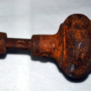 May include: An antique door knob set with a heavily rusted, aged appearance. The door knob has a rounded, bulbous shape with a decorative pattern. The connecting rod and the knobs are covered in orange-brown rust.