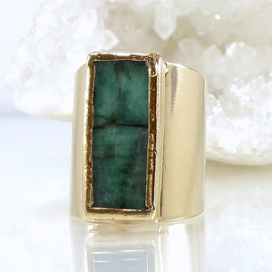 May include: A gold ring with a large, rectangular emerald green gemstone set in a gold bezel.