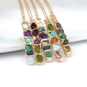 May include: Five gold necklaces with different colored gemstones. Each necklace has a long, thin pendant with a hammered texture and a row of small, colorful gemstones.