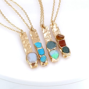 May include: Four gold necklaces with hammered bar pendants featuring different colored gemstones. The gemstones include turquoise, opal, aquamarine, and carnelian.