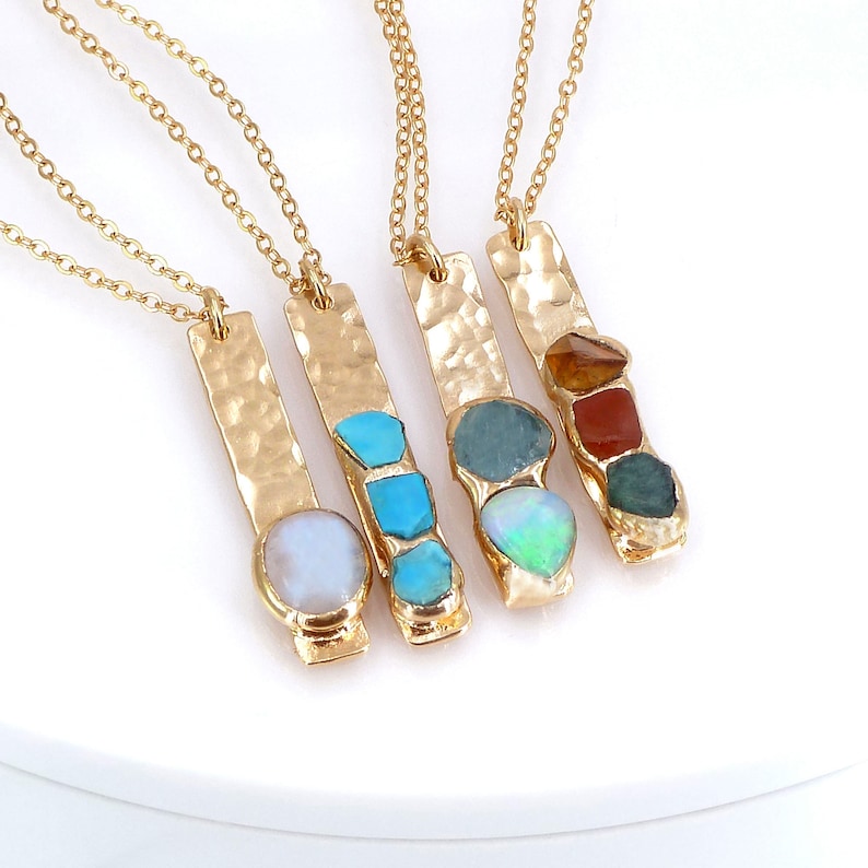 May include: Four gold necklaces with hammered bar pendants featuring different colored gemstones. The gemstones include turquoise, opal, aquamarine, and carnelian.