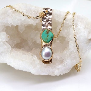 May include: A gold chain necklace with a hammered gold bar pendant featuring a turquoise gemstone and a white pearl.