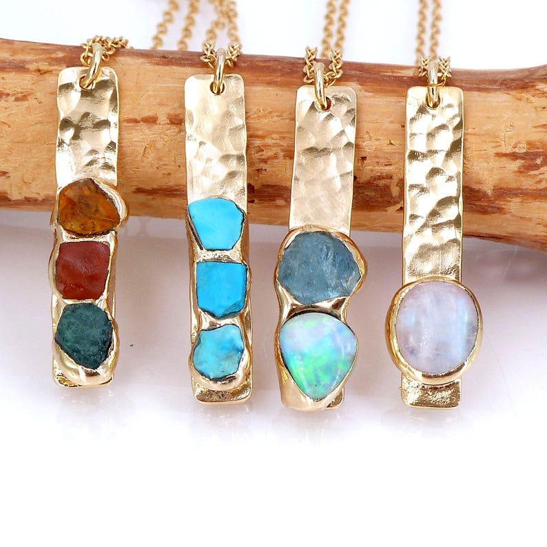 May include: Four gold necklaces with different gemstone pendants. The pendants are set in hammered gold bars. The gemstones include turquoise, opal, moonstone, and a mix of red, orange, and green stones.