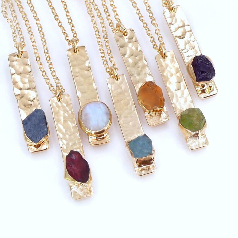 May include: A set of nine gold necklaces with hammered bar pendants and various gemstone accents. The gemstones include amethyst, aquamarine, citrine, garnet, green aventurine, moonstone, peridot, ruby, and sapphire.