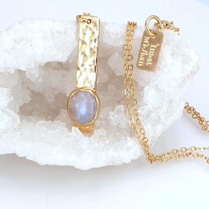 May include: Gold necklace with a hammered bar pendant and a moonstone gemstone. The necklace also features a small tag with the text "Lunar Mi-Shau".