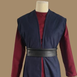 May include: A long, dark blue sleeveless vest with a black leather belt. The vest is open at the front and has a deep V-neck. The vest is worn over a long-sleeved, burgundy shirt.