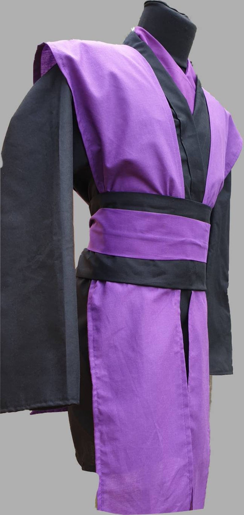 Puede incluir: Una t&uacute;nica morada y negra con una faja ancha. La t&uacute;nica tiene mangas largas y cuello en V.