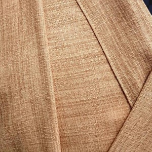 May include: Close-up of a brown fabric with a textured weave. The fabric is folded over itself, creating a diagonal line.