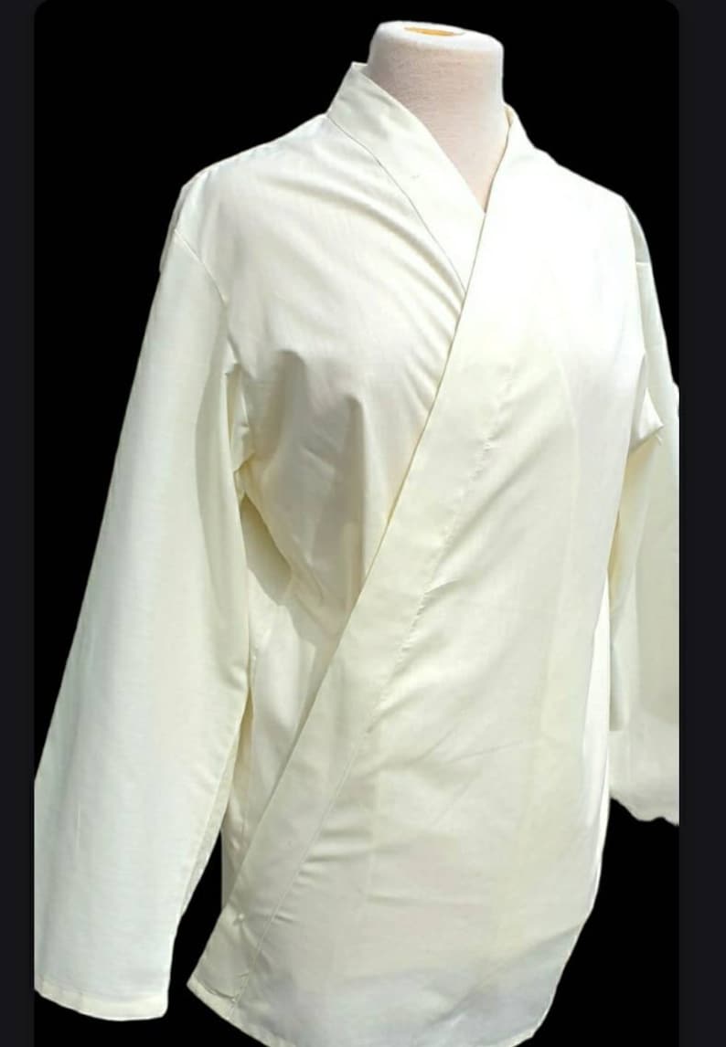 May include: A white long-sleeved shirt with a mandarin collar and a wrap-style closure. The shirt is made of a lightweight fabric and has a relaxed fit.