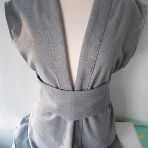 May include: A gray sleeveless cardigan with a deep V-neck and a self-tie belt.