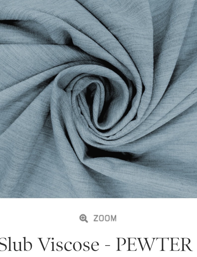 May include: Close-up of a soft, blue, textured fabric with a slub weave. The fabric is folded and twisted, creating a swirling pattern. The fabric is called "Slub Viscose - Pewter".