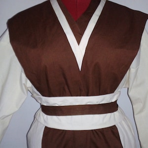 May include: A brown and white tunic with a V-neck and a brown belt. The tunic has a long sleeve and a collar.