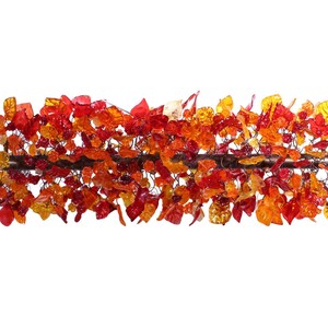 May include: A glass sculpture of a branch with red, orange, and yellow leaves. The leaves are made of glass and are arranged in a cascading pattern.