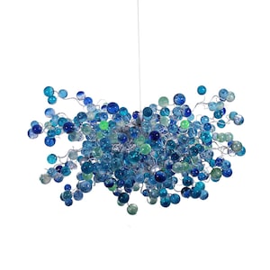 Puede incluir: Una lámpara de araña moderna con un grupo de orbes de vidrio azul y verde suspendidos de un marco de alambre plateado.