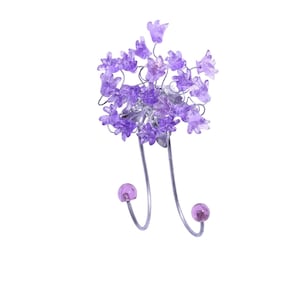 Könnte beinhalten: Ein doppelter Wandhaken in Form einer lila Blume. Der Haken ist aus Metall und hat zwei Zacken. Die Blumen sind aus Glas und haben eine helllila Farbe.