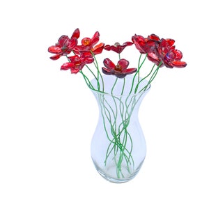 May include: A bouquet of red glass flowers in a clear glass vase. The flowers have a shiny finish and are arranged in a simple, elegant design.