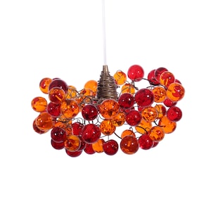 May include: A modern chandelier with a cluster of red and orange glass spheres hanging from a wire frame.