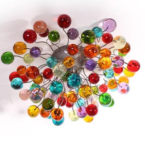 Könnte beinhalten: Ein farbenfroher Glas-Kronleuchter mit einer Vielzahl von runden, kugelförmigen Glaskugeln in verschiedenen Farben, darunter Rot, Orange, Gelb, Grün, Blau und Lila. Die Kugeln sind an einer zentralen Metallstruktur befestigt.