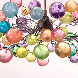 May include: A chandelier featuring multiple glass spheres in shades of pink, orange, green, blue, and purple. The spheres are attached to a dark metal frame, forming a decorative light fitting.