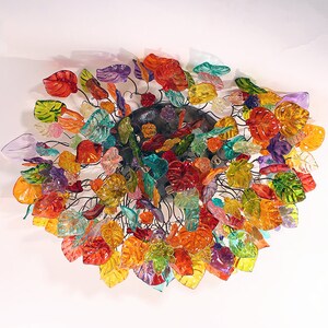 Puede incluir: Una lámpara de araña de hojas de vidrio de colores, con una variedad de colores, incluyendo rojo, naranja, amarillo, verde, azul y morado.